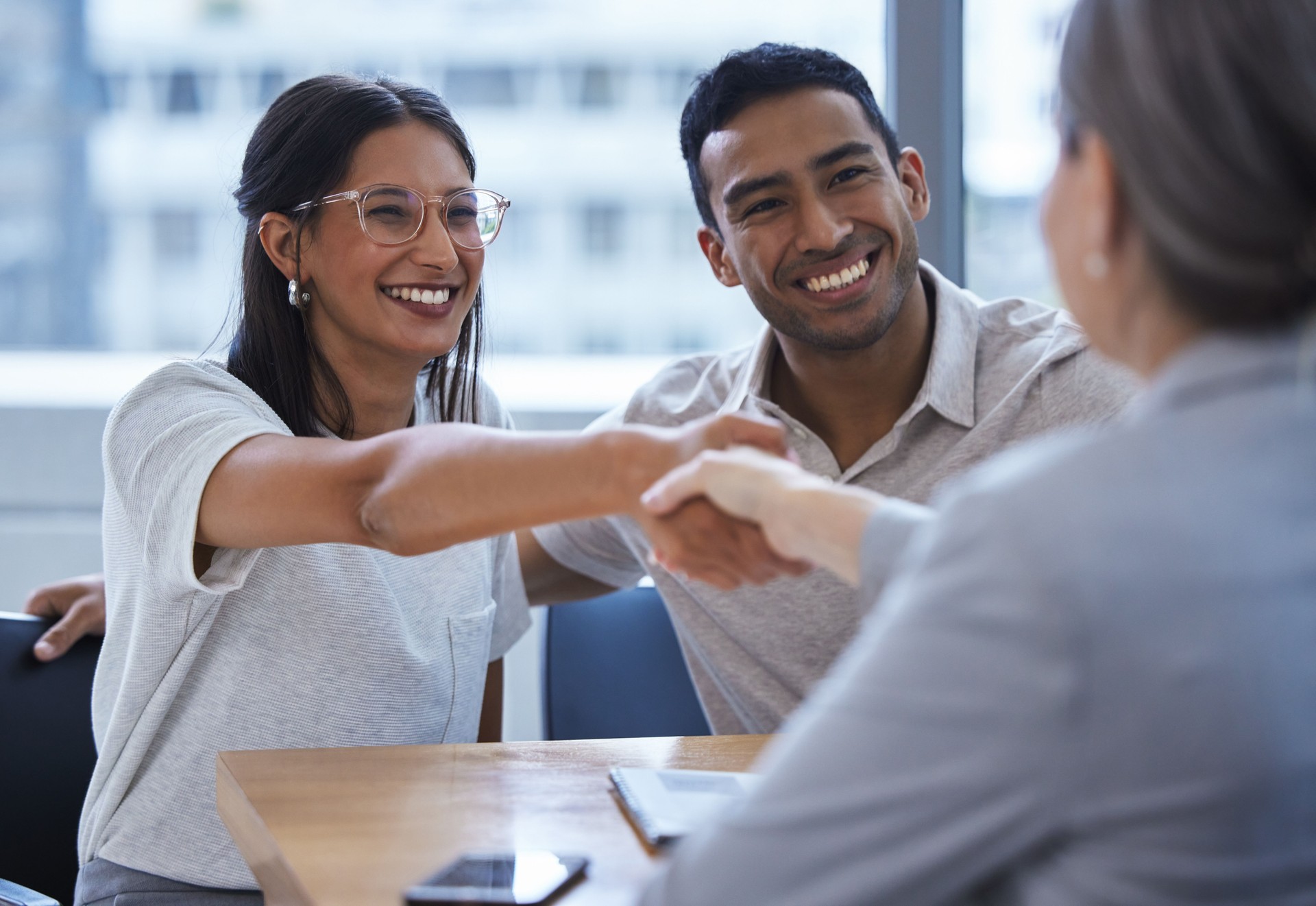 Shot of a young couple sharing a handshake with a consultant they're meeting to discuss paperwork an office